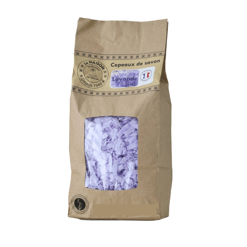 A brown paper bag with a clear window reveals purple Savon de Marseille Lavender Soap Flakes from French Soaps. The label displays "Copeaux de savon" and "Lavande," featuring Provence lavender scent and natural ingredients.
