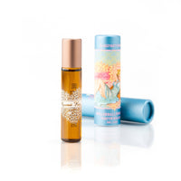 A small rollerball perfume labeled "Barefoot Venus Coconut Kiss Roll on Perfume" stands in front of a light blue cylindrical container with an illustration of a woman lying on a beach. The cruelty-free perfume, enriched with jojoba oil, has a gold cap, and the background is plain white.