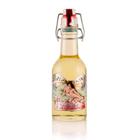 A small glass bottle with a swing-top lid, containing Barefoot Venus The Vanilla Effect Body+Bath+Massage Oil, a pale yellow liquid infused with natural oils. The label showcases an illustration of a fairy with wings and floral elements, highlighting its cruelty-free essence.