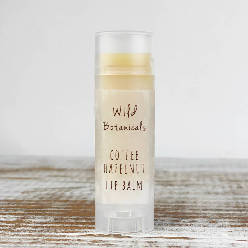 A tube of Wild Botanicals - Coffee Hazelnut Lip Balm standing on a rustic wooden surface. The label is clear with black and brown text and mentions its content of organic jojoba.