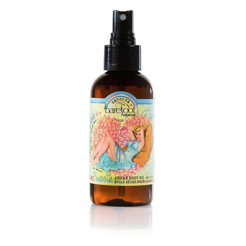 A brown spray bottle labeled "Barefoot Venus" with a colorful illustration of a lounging woman surrounded by pink and yellow flowers. The label highlights the product as "Barefoot Venus Coconut Kiss Argan Body Oil" made with nourishing Argan Oil and all-natural ingredients.