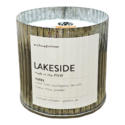 The Anchored Northwest Lakeside Rustic Vintage Farmhouse Wood Wick Candle in a ribbed metallic holder features eco-friendly soy wax and notes of ozone, linen, eucalyptus, sea salt, freesia, moss, and powder. Crafted with care in Spokane, WA, it's perfect for any home decor.