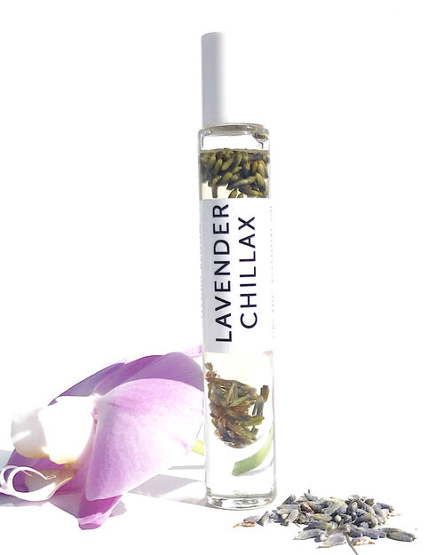A glass roller bottle labeled "Hydra Bloom Beauty Lavender Chillax Organic Essential Perfume oil" with dried lavender buds inside, a white cap, accompanied by a fresh orchid flower and loose lavender buds beside it on a white background. This Hydra Bloom Beauty Lavender