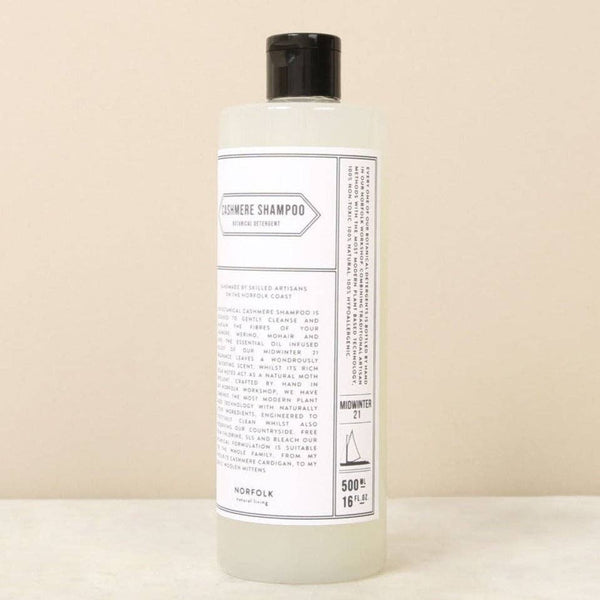 A clear plastic bottle with a black cap holds 500ml of Norfolk Natural Living Cashmere Shampoo, formulated for delicate knitwear. The label features product details and instructions. The Norfolk Natural Living bottle rests on a neutral beige background.