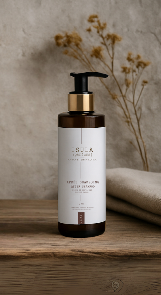 A bottle of ISULA parfums Isula Fiore di Castagna - Chestnut Flower Hair Conditioner with a black pump sits on a wooden surface next to beige towels, dried flowers in the background evoking a minimal, natural feel and revived hair shine.