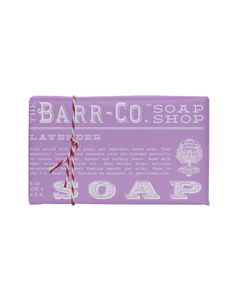 Introducing the Barr-Co. Lavender Triple Milled Bar Soap by K. Hall, a soothing lavender-scented soap bar. The packaging features a purple design accented with white text that details the ingredients and benefits, including shea butter and natural olive oil, while proudly being free of parabens. For an added decorative touch, one end of the bar is tied with red and white twine.