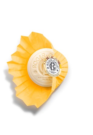 A round beige Roger & Gallet Orange Wood Wellbeing Soap (3.5 oz) is embossed with "Roger & Gallet Paris," partially wrapped in bright yellow pleated paper, and topped with a round white logo label. Set contains 3 soaps.