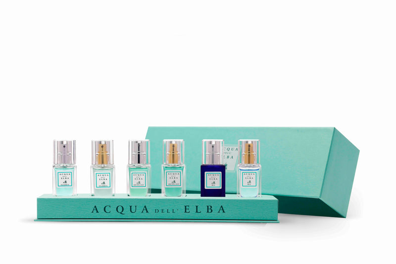 The Acqua dell'Elba Preziosa Discovery Gift Box features six fragrances—five clear and one deep blue—displayed on a teal tray with a matching box behind. Both the bottles and tray display the Acqua dell'Elba brand name.