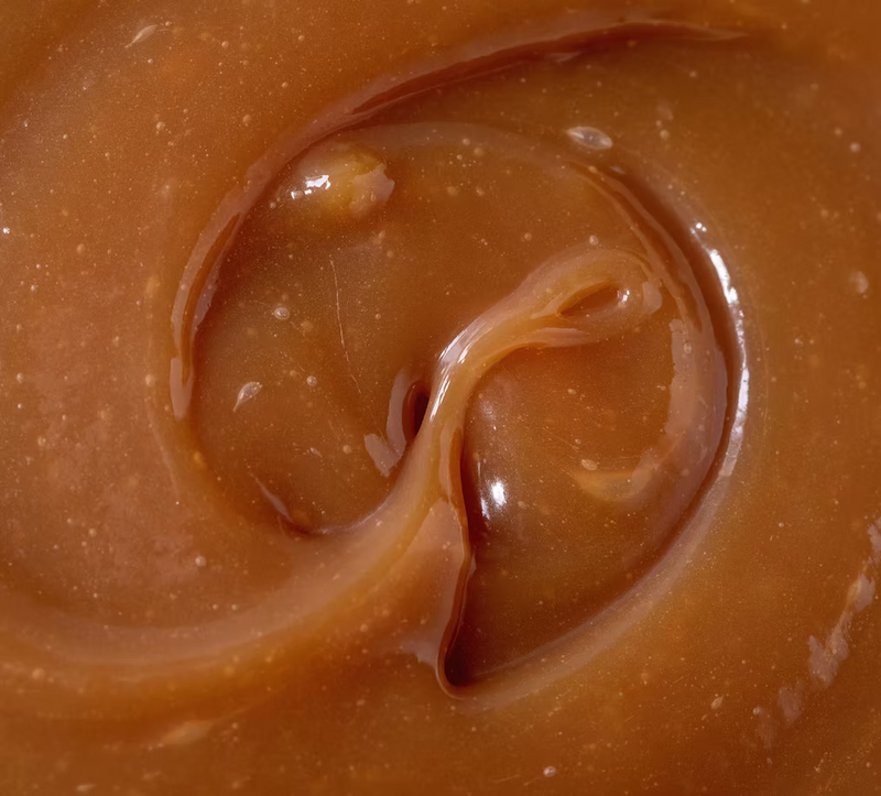 A close-up of glossy caramel sauce swirled like amber, its rich, creamy look echoing the elegance of ISULA parfums Room Diffuser - Isula Inzuccarata - Sweet Island No.23.