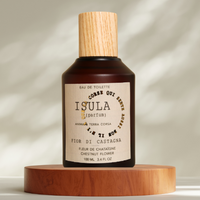 A brown glass bottle with a wooden cap, labeled "ISULA parfums Chestnut Flower eaux de toilette," rests on a round beige platform. The Corsican fragrance is softly lit, with gentle shadows in the background.