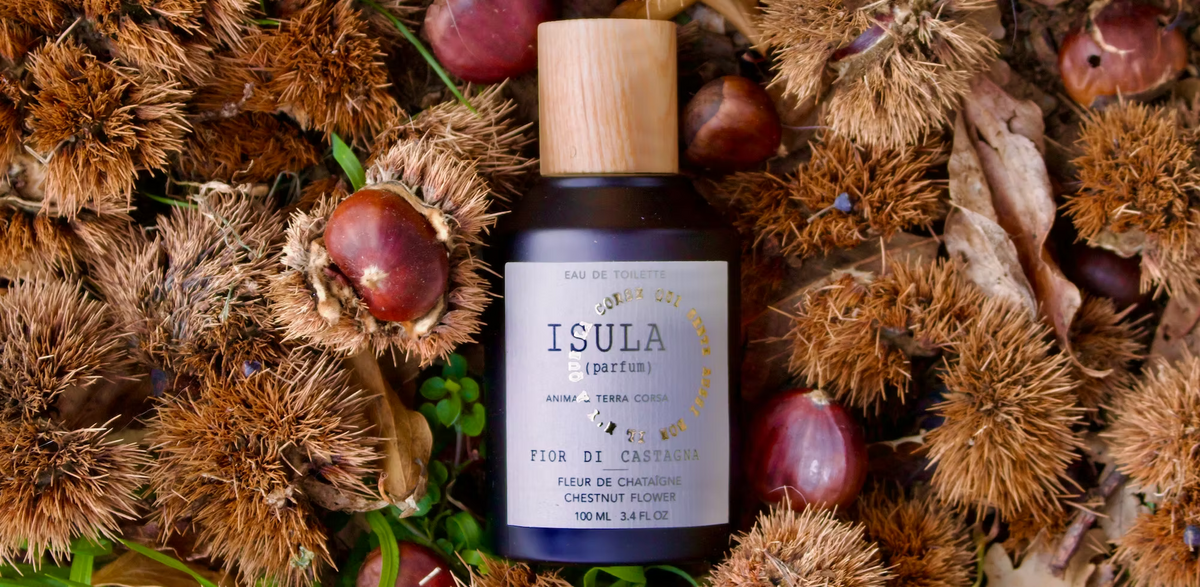 A bottle of ISULA parfums Chestnut Flower eaux de toilette sits on chestnut shells and leaves. The label reads “Fior di Castagna.” This Corsican scent by ISULA parfums channels nature’s earthy, botanical essence.
