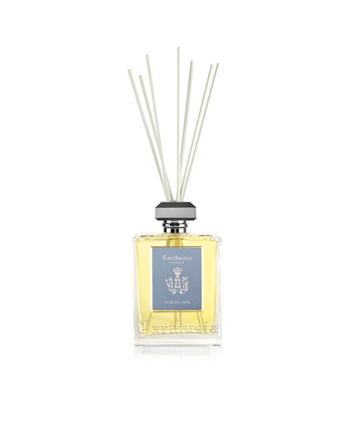 The Carthusia I Profumi de Capri Fiori di Capri Reed Diffuser (230ml) features a clear glass bottle with light yellow liquid, gray cap, white reeds, and a blue label to beautifully enhance your home's fragrance and décor.