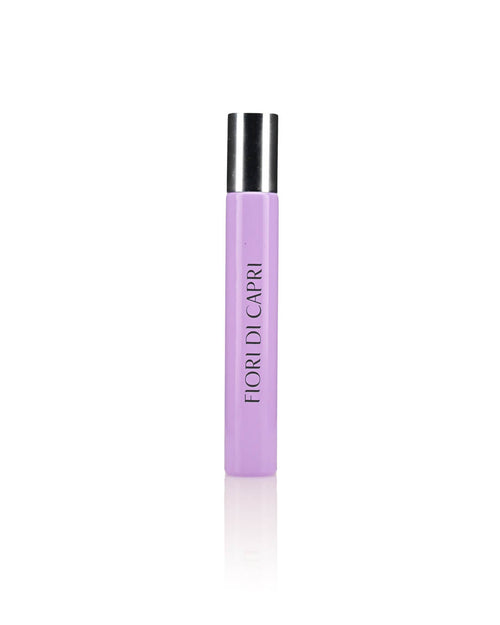 A lavender-colored cylindrical perfume bottle with a silver cap, adorned with the text "FIORI DI CAPRI" printed vertically on the front, radiates the enchanting Flowers of Capri scent. The white, plain background accentuates its elegance. Perfect for your Carthusia Fiori di Capri Travel Clutch Bag by Carthusia I Profumi de Capri.