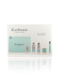 A boxed set of "Carthusia Via Camerelle Travel Clutch Bag" by Carthusia I Profumi di Capri featuring a turquoise zipper pouch and four bottles of various perfumes and toiletries displayed in front of the pouch. The packaging, inspired by the Capri fragrance, is minimalist with white and turquoise accents.