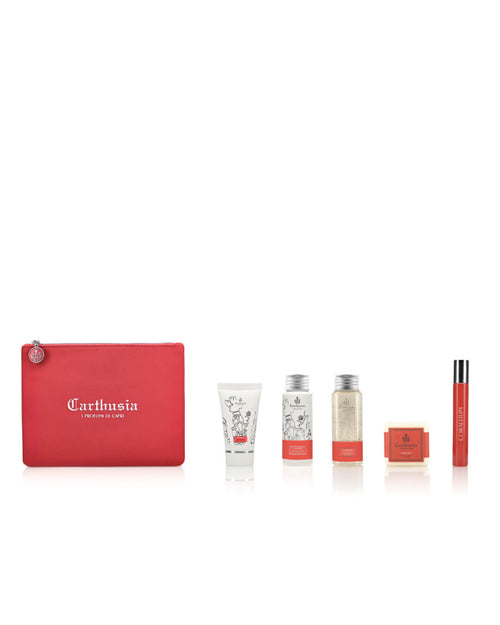 A red Carthusia I Profumi di Capri-branded Carthusia Corallium Travel Clutch Bag is placed on the left. To the right of the pouch, there are several beauty products: a white tube, a cylindrical container with a detailed label of Carthusia Corallium, a box, a rectangular container, and a slim spray bottle.