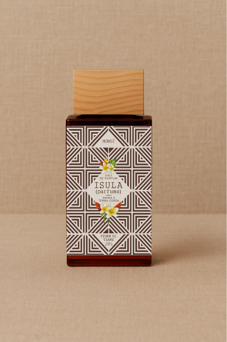 A rectangular ISULA parfums Fiore di Tiare eau de parfum bottle with a light wooden cap and geometric black and white floral label sits on a beige textured background. The label displays "ISULA parfums," evoking an exotic Monoi-infused scent.