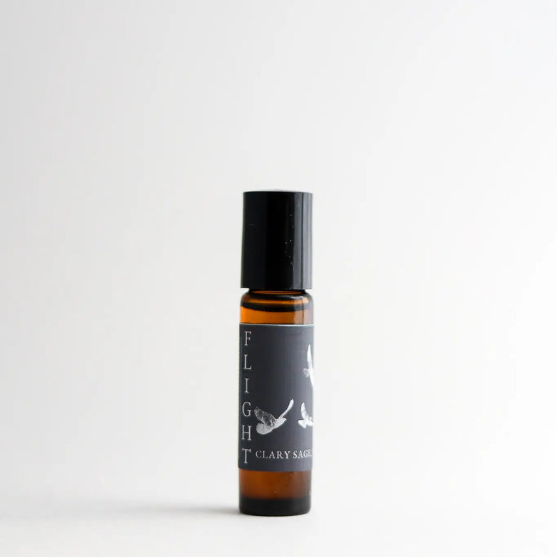 A clear bottle of Nustad Family Ranch Flight Essential Oil Perfume Roller with a black cap, standing against a plain white background. The label features a minimalistic bird design and mentions it contains organic jojoba oil.