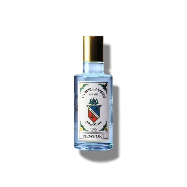 A clear glass bottle of Caswell-Massey Newport Aftershave with a gold cap and vibrant crest label sits against a white background with a soft shadow—offering a refreshing touch after shaving.