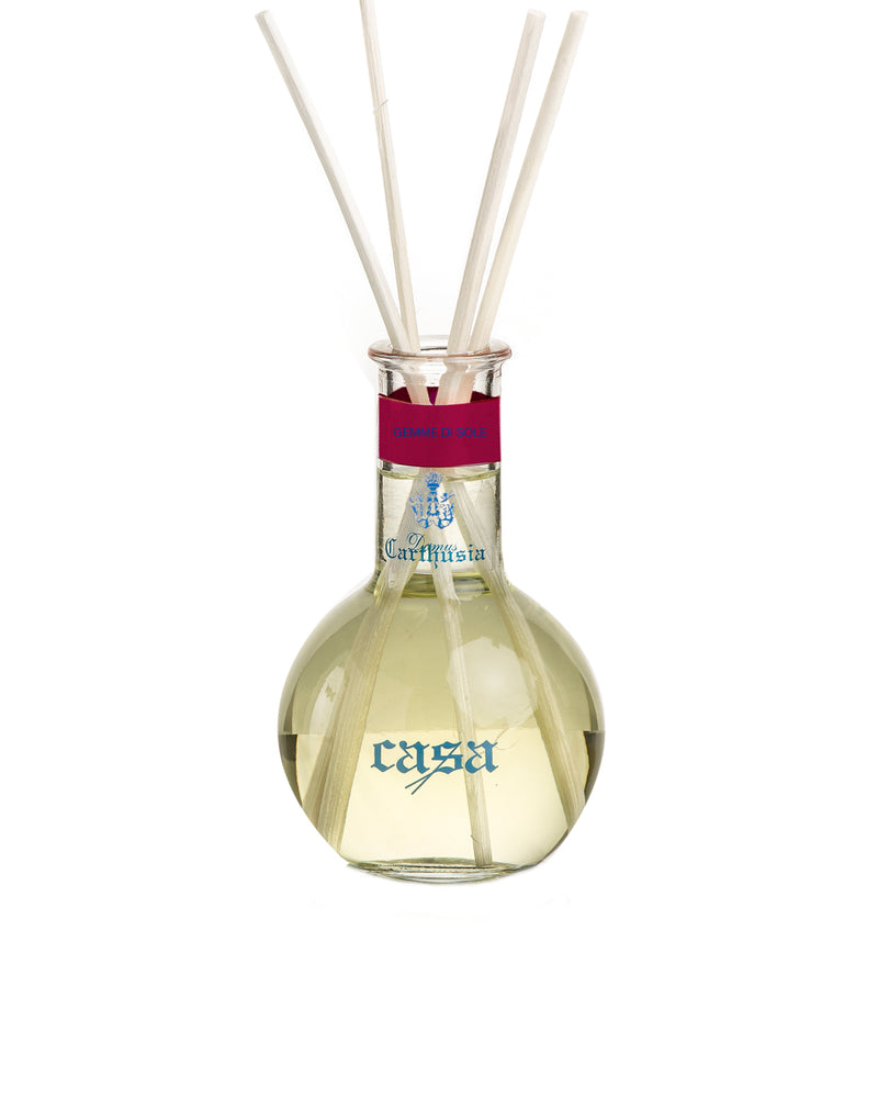 A Carthusia Gemme di Sole Reed Diffuser 100ml diffuser with a clear, rounded bottle containing yellow liquid and three white diffuser sticks. The label on the bottle reads "Carthusia I Profumi de Capri".