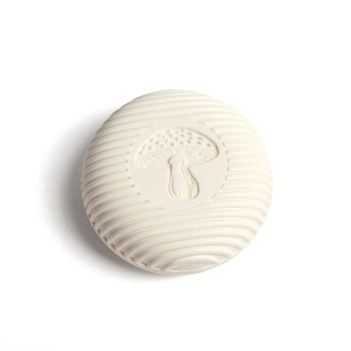 A round, cream-colored soap featuring a textured surface and an embossed mushroom design on top captures the allure of Kala's Swedish Dream Gnome Soap.