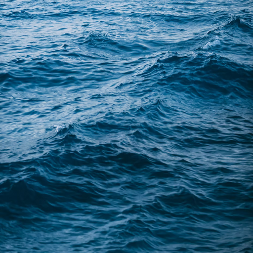 A close-up of gently rippling blue ocean water reflects the essence of ISULA parfums Storia di Mare - Sea Story, capturing an aquatic fragrance with crisp marine musk by ISULA parfums.