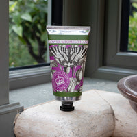 A tube of The English Soap Co. Kew Gardens Elderflower and Pomelo Hand Cream with a floral design stands upright on a marble windowsill, radiating luxury as greenery appears through the window in the background.