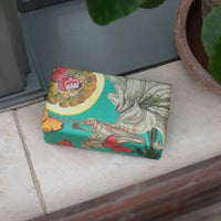 The English Soap Co. Kew Gardens Grapefruit and Lily Soap, in colorful botanical packaging, rests on a tiled floor near a plant pot and window. The vegan bar features grapefruit and lily illustrations and The English Soap Co. branding.