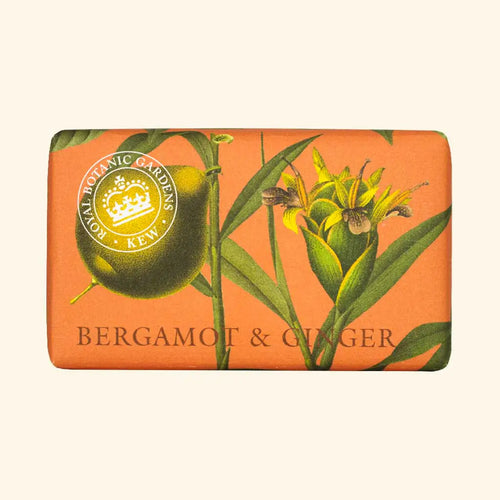 A bar of The English Soap Co. Kew Gardens Bergamot and Ginger Soap wrapped in orange paper adorned with botanical illustrations of bergamot fruit and ginger flowers. This vegan-friendly soap's packaging features the yellow and white emblem of Royal Botanic Gardens, Kew, and "BERGAMOT & GINGER" printed in black at the bottom, promising a luxurious bathing experience.