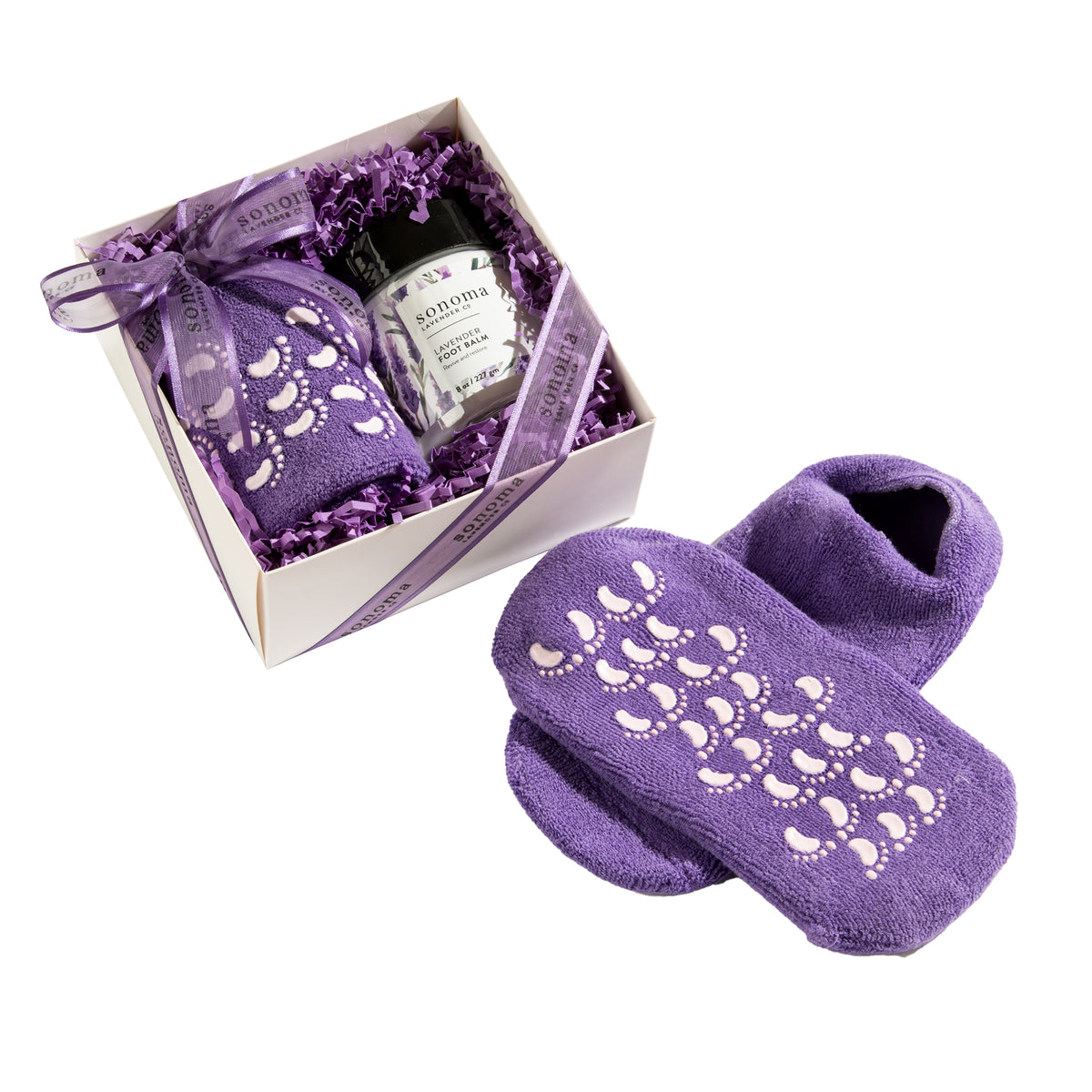 The Sonoma Lavender Hydrating Socks & Lavender Foot Balm gift set by Sonoma Lavender includes a pair of purple hydrating socks with a non-slip pattern and is complemented by relaxing scented candles and a soothing foot balm, all beautifully presented in a white box with a purple ribbon.