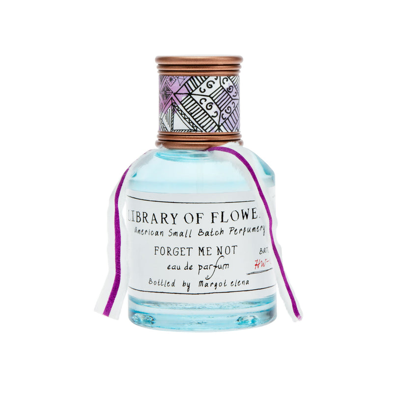 A bottle of Margot Elena's "Library of Flowers Forget Me Not Eau De Parfum" with a clear blue liquid, decorative tribal patterns on the cap, and a purple ribbon tied around the neck, isolated.