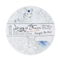 Round container of Margot Elena's Library of Flowers Forget Me Not Parfum Crema featuring delicate illustrations of blue foxes and floral patterns on a white background.