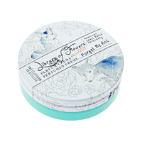 Round container of Margot Elena's Library of Flowers Forget Me Not Parfum Crema with delicate floral illustrations in blue and white on the lid. Text on the top includes product details.