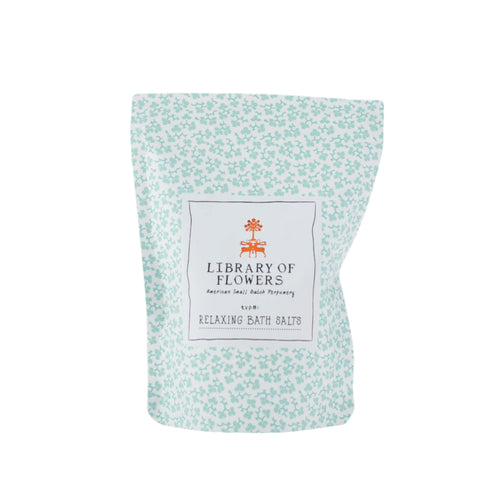 The "Library of Flowers True Vanilla Salts" by Margot Elena features a white and light blue floral-patterned pouch, accented with a small orange flower logo. Infused with mineral-rich sea salts and floral essences, this bath blend offers a serene escape.