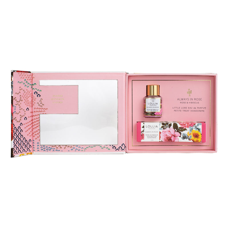 The Lollia Always in Rose Fragrance Story Gift Set by Margot Elena comes in a decorative floral box and includes a small bottle of Eau de Parfum labeled "Always in Rose." The interior boasts a pink and silver design with intricate patterns on the left side, making it ideal for pairing with our Shea Butter Handcreme.