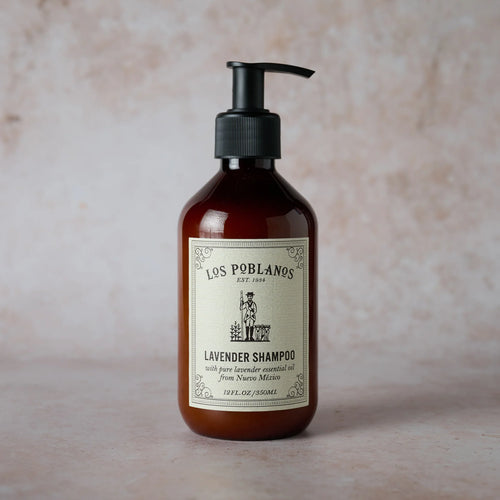 A brown pump bottle of Los Poblanos Lavender Shampoo, featuring a cream label with black text and an illustration, is shown on a light, textured surface.