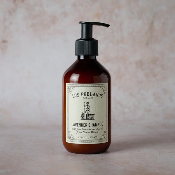 A brown pump bottle of Los Poblanos Lavender Shampoo, featuring a cream label with black text and an illustration, is shown on a light, textured surface.
