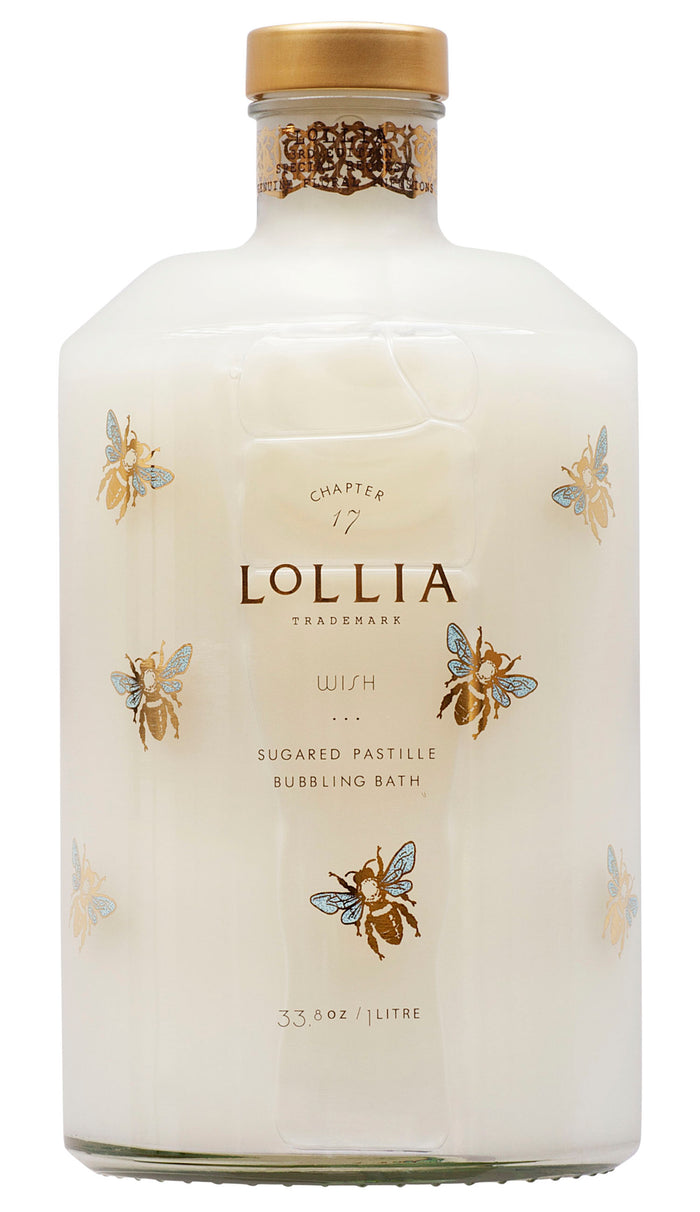 A clear bottle of Margot Elena Lollia Wish Bubble Bath with gold and blue bee illustrations, filled with milky-white liquid rich in Olive Fruit Oil, and topped with a gold cap.
