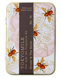 A decorative Margot Elena tin featuring artistic white floral designs with gold accents and bees, labeled "eau de parfum little luxe petite treat no. 10 honey & the moon," with TokyoMilk Honey & The Moon Flirt With Me Fragrance Kit.