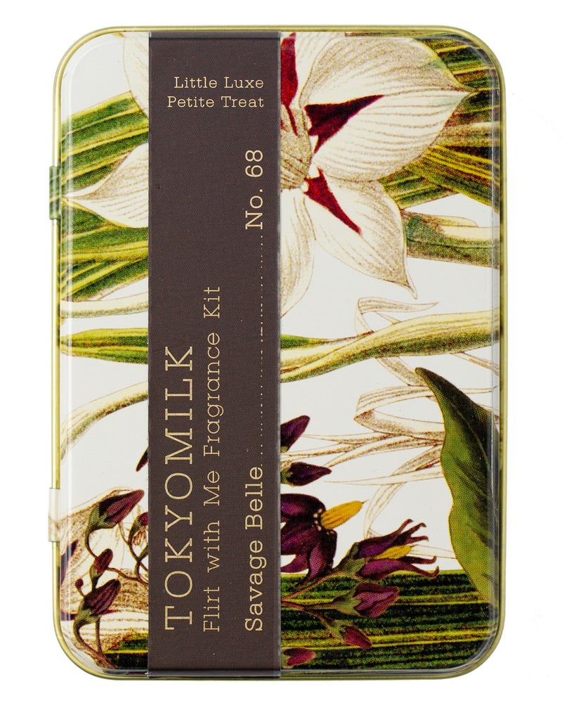 A decorative tin labeled "Margot Elena TokyoMilk Savage Belle Flirt With Me Fragrance Kit," featuring floral artwork with orchids and green leaves.