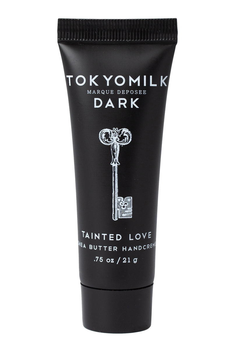 A black tube of Margot Elena TokyoMilk Tainted Love Travel Size Hand Creme with sandalwood and dark vanilla bean, featuring a vintage key design, isolated on a white background.