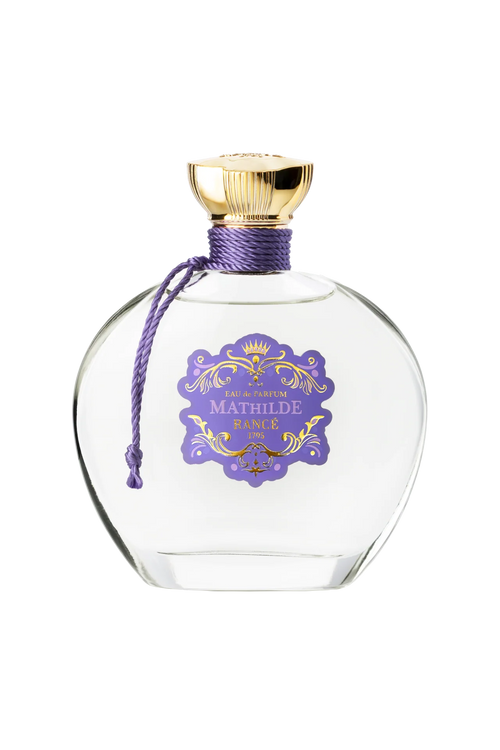 Rancé Mathilde Eau de Parfum - 100ml by Rancé comes in a clear glass bottle with a gold cap, purple cord, and ornate label, offering a refined floral woody fragrance that captures timeless elegance.
