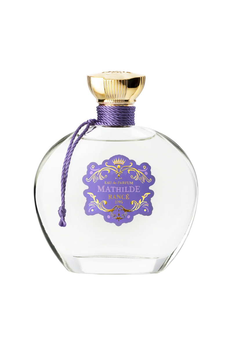 Rancé Mathilde Eau de Parfum - 100ml by Rancé comes in a clear glass bottle with a gold cap, purple cord, and ornate label, offering a refined floral woody fragrance that captures timeless elegance.