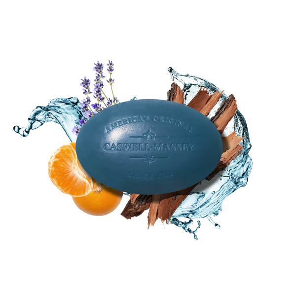 A blue oval Caswell-Massey Newport Bar Soap is displayed on a white background with water splashes, lavender sprigs, an orange slice, and wood, highlighting its coastal fragrance and luxurious triple-milled formula.