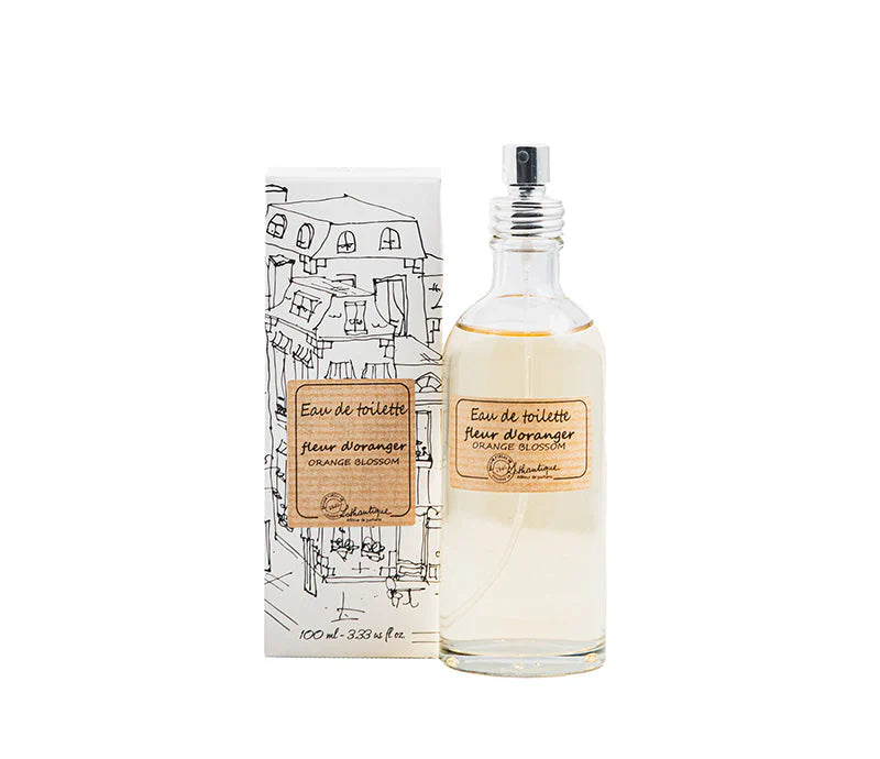 A clear glass bottle of Lothantique Orange Blossom Eau de Toilette, a French floral fragrance, stands beside its white box decorated with black city buildings. The bottle features a spray nozzle and a simple beige label.