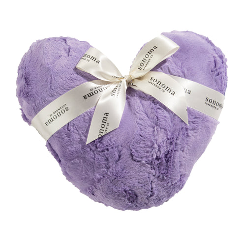 A plush purple heart-shaped pillow tied with a cream-colored ribbon printed with the word "Sonoma" multiple times. The fabric texture of the Sonoma Lavender Comforting Heart Pillow Bellflower Rose appears soft and fluffy.