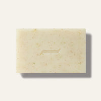 The Caswell-Massey Patchouly and Pine Bar Soap by Caswell Massey is a rectangular, off-white botanical soap with brown and green specks and a curved center indentation, displayed on a light background.