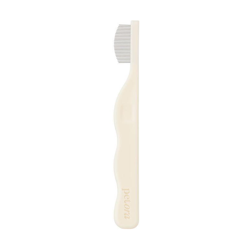 The Petora BRUSH ON ME Pet Facial & Eye Comb is a beige grooming tool with fine metal teeth and an ergonomic handle, embossed with "Petora," perfect for precise tear stain removal and facial grooming, shown in profile on a white background.