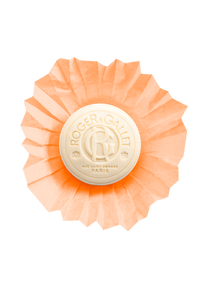 A circular Roger & Gallet Carnation soap bar in an orange-coral hue, featuring intricate embossed designs and a floral fragrance, with the brand logo centered within a regal frame, against a matching background.