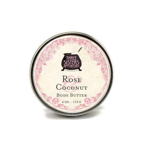 A tin labeled "Three Sisters Aphothecary Rose Coconut Body Butter" (4 oz/113g) with a pink floral border highlights this natural skincare shea butter moisturizer against a white background.