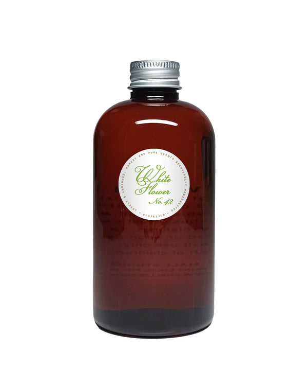 A brown glass Simpatico White Flower Hobnail Diffuser Refill bottle with a silver screw cap and white label is shown on a plain white background, offering a subtle floral fragrance.
